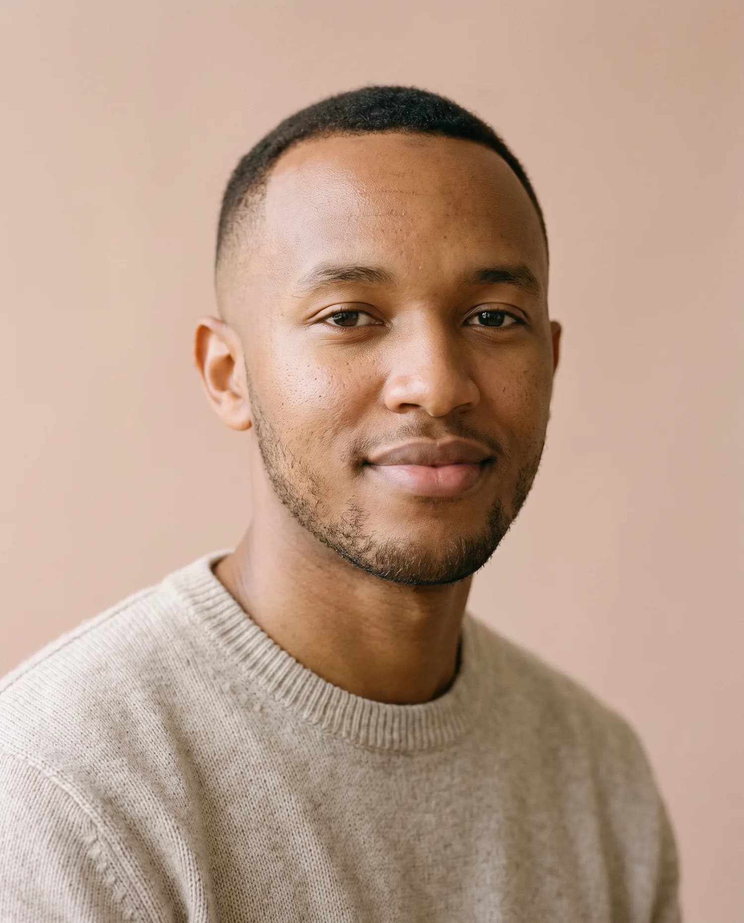 Campaign image: a young man with clear light-brown skin and a short fade, in an oatmeal knit, soft window light